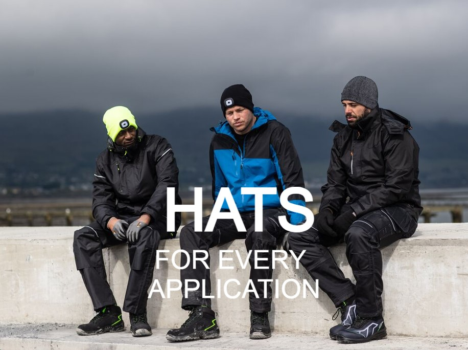 Image of three men in different work clothes. All three are wearing hats on their heads and are sitting on a concrete wall. In the background you can see a cloud-covered mountain and gray fog. A link to our selection of hats is provided.