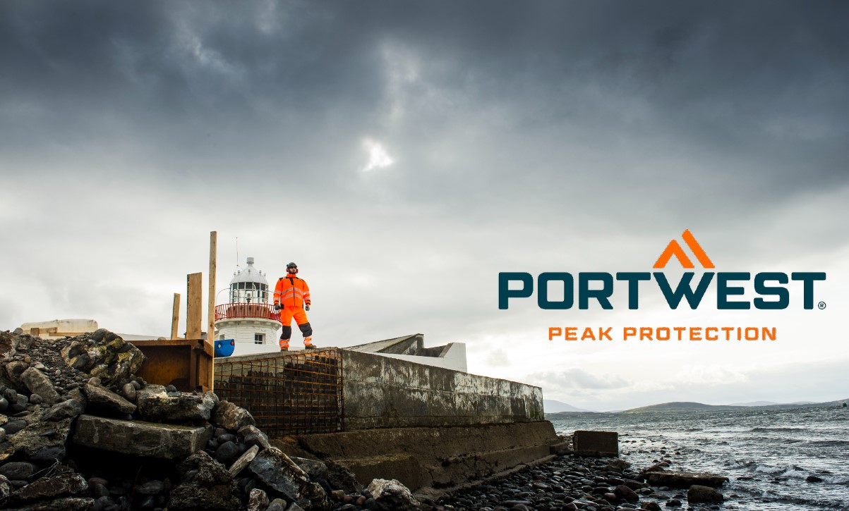 A worker in orange high visibility clothing stands on a rocky construction site next to a lighthouse, with the Portwest logo and the slogan 'Peak Protection' in the picture. A link is provided that leads to our multinorm workwear.