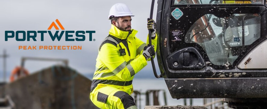 A worker in a bright yellow high-visibility suit with reflective stripes, a white safety helmet and gloves climbs into a construction machine. In the background you can see a construction site environment with construction equipment and a gray sky. At the top left of the picture is the "Portwest" logo with the slogan "Peak Protection".