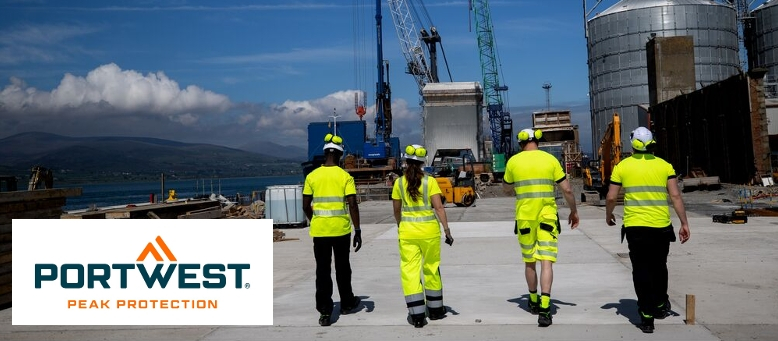 Four workers in yellow high-visibility clothing in front of a backdrop of silos and cranes. In the background you can see a mountain range and a blue sky with a few white clouds. In the bottom left of the picture is the Portwest logo in blue and orange on a white background.