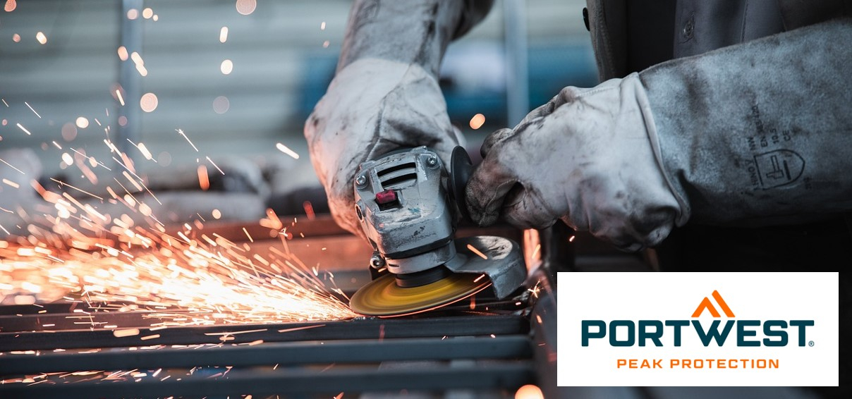 The image shows a worker working on metal with a grinder. Sparks fly from the grinding wheel, indicating intensive work. The worker is wearing thick protective gloves and special protective clothing to protect himself from sparks and heat. In the lower right area of ​​the image you can see the logo of Portwest, a manufacturer of protective clothing, with the slogan "Peak Protection".