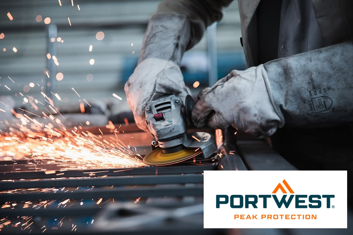 The image shows a worker working on metal with a grinder. Sparks fly from the grinding wheel, indicating intensive work. The worker is wearing thick protective gloves and special protective clothing to protect himself from sparks and heat. In the lower right-hand part of the image you can see the logo of Portwest, a manufacturer of protective clothing, with the slogan "Peak Protection". An article about our flame-retardant clothing is included.