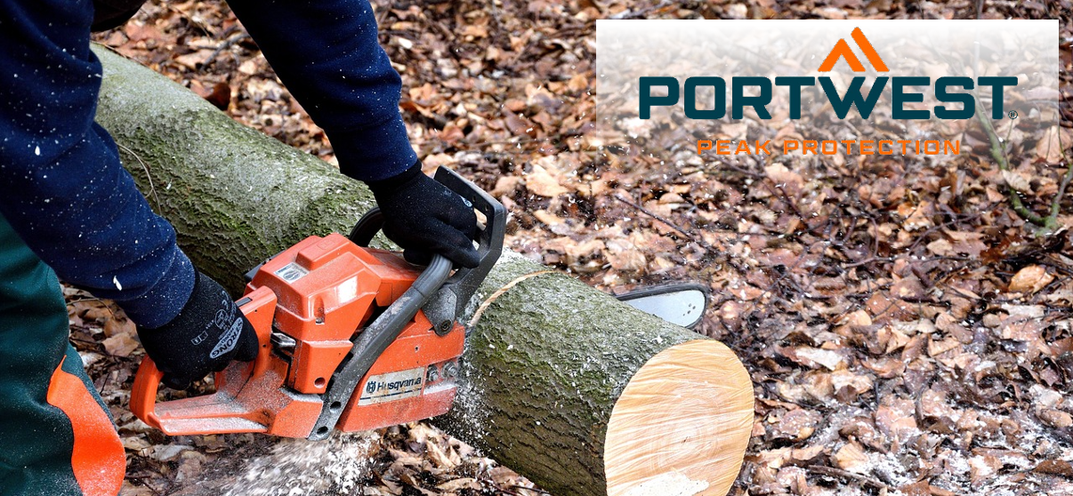 A person is seen using a chainsaw to saw through a tree trunk lying on the ground. In the background you can see brown autumn leaves and flying wood chips. In the upper right corner of the image is the Portwest logo in blue and orange against a transparent white background.