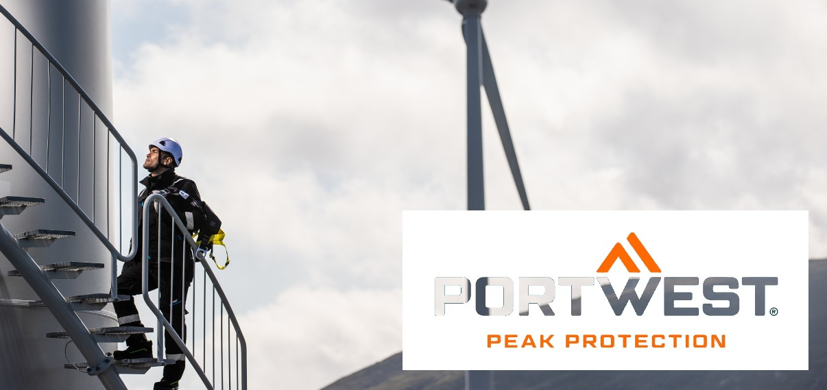 Worker in protective clothing climbing a wind turbine using a spiral staircase. In the background you can see grey clouds, mountains and another wind turbine. In the bottom right of the picture is the Portwest logo in white and orange.